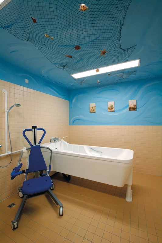 Pflegebad mit Badewanne unter blauer Decke, an der zur Zierde ein Fischernetz hängt.