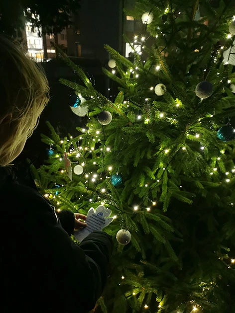 Eine Frau liest einen Wunsch von einem Zettel ab, der am Tannenbaum hängt.