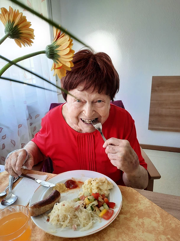 Eine Bewohnerin isst Bratwurst mit Salat und lacht in die Kamera.