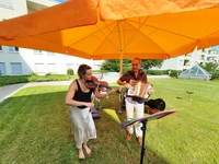 Musiker mit Akkordeon und Musikerin mit Geige unter einem Sonnenschirm in Orange.