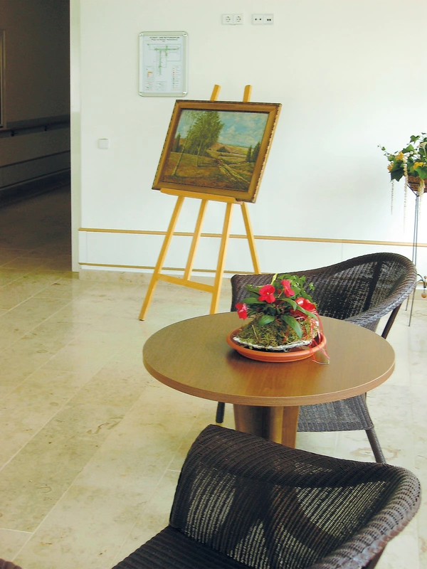 Café Kochstedt, ein runder Holztisch mit Blumengesteckt, zwei Designerstühle, im Hintergrund ein Bild auf einer Staffelei.