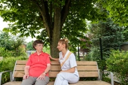Auf einer Bank unter einem Baum im Garten unterhalten sich eine Bewohnerin und eine Mitarbeiterin.