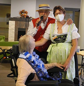 Sänger Hans-Harald mit einer Mitarbeiterin im Dirndl und einer Bewohnerin im Rollstuhl.