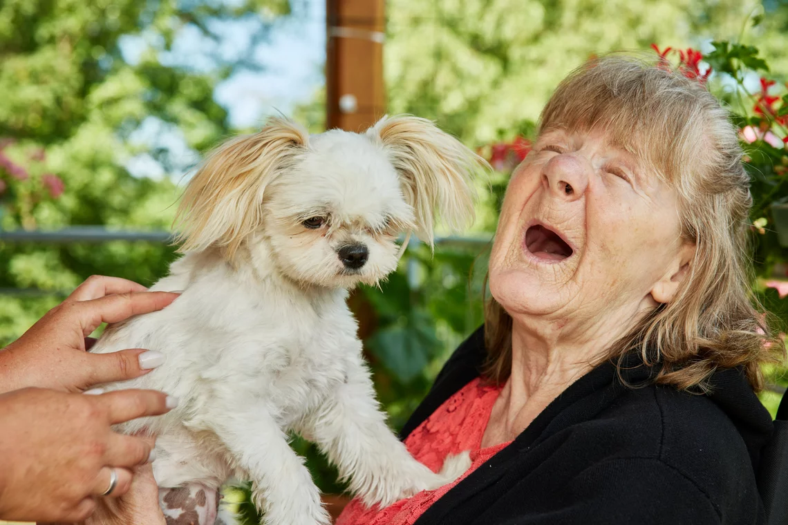 Eine Bewohnerin lacht, weil ein kleiner Hund ihr Freude bereitet