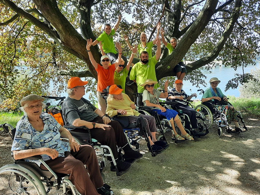 Gruppenfoto, vorn Bewohner im Rollstuhl, dahinter Mitarbeiter, die zum Teil im Baum sitzen