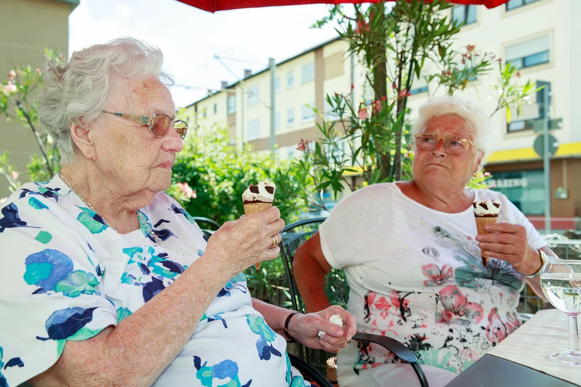 Zwei Seniorinnen genießen ein Eis unterm Sonnenschirm.