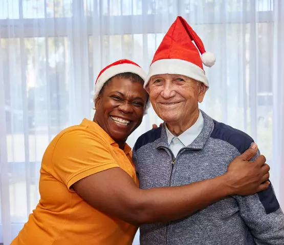 Eine Mitarbeiterin und ein Bewohner tragen Nikolausmützen lachen