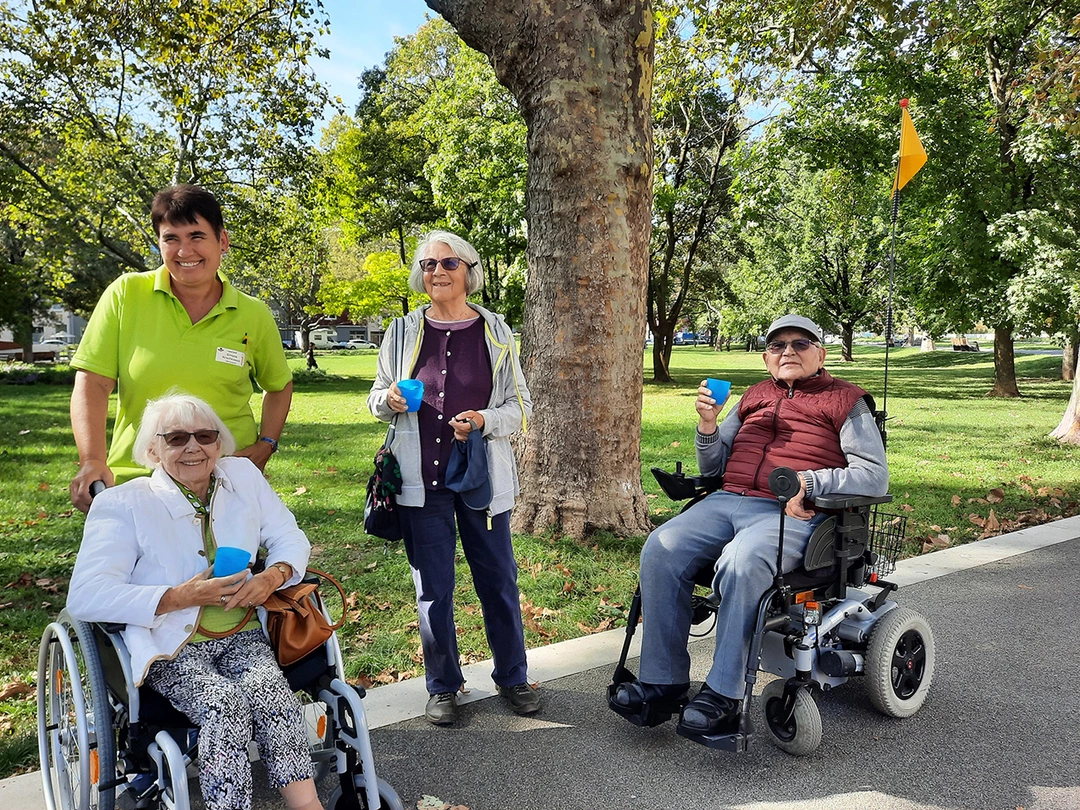 Mitarbeiter mit Bewohnern im Rollstuhl im Park