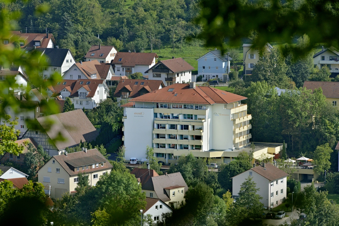 Einrichtung Am Mühlbach aus der Ferne inmitten von Mehrfamilienhäusern und vielen Bäumen, im Hintergrund eine Wiese und Wald.
