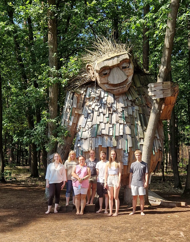 Schüler im Wald vor einer riesigen Holzfigur