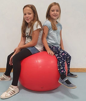 Zwei Mädchen sitzen auf einem großen Ball.