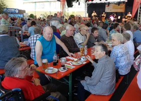 Viele Bewohner bei einem Ausflug auf den Fohlenmarkt; sie sitzen an Bierbänken, essen, trinken und hören der Band zu.