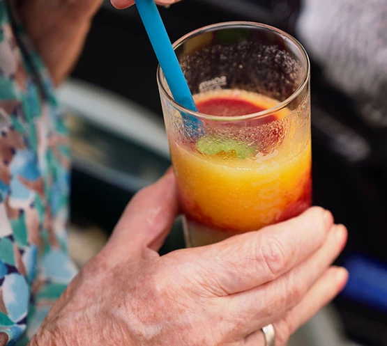 Die Hand einer Seniorin hält einen Sommerdrink mit Strohhalm.