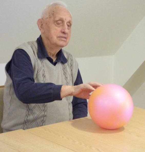 Ein Senior stößt mit der linken Hand einen roten Ball an und rollt ihn über den Tisch.