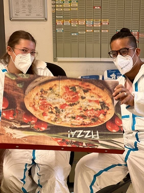 Zwei Mitarbeiter machen freudig einen Pizzakarton auf.