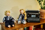 Vor einer alten Schreibmaschine sitzen zwei Püppchen