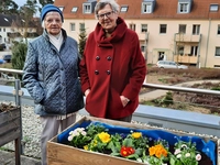 Zwei Bewohnerinnen hinter einem mit Frühlingsblühern bepflanzten Hochbeet