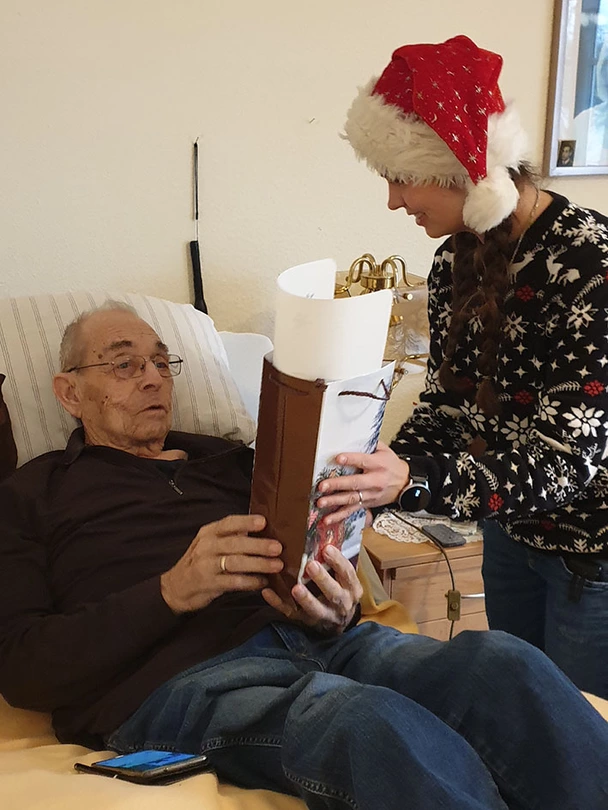 Bewohner erhält Geschenk von Mitarbeiterin mit Nikolaus-Mütze