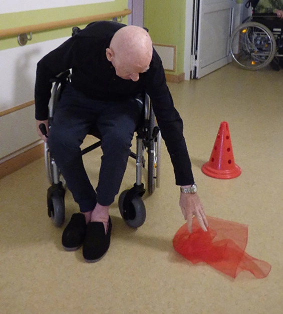 Ein Mann im Rollstuhl bückt sich nach einem Tuch am Boden.