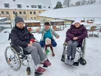 Mitarbeiterin kniet hinter einem kleinen Schneemann, zwei Bewohnerinnen im Rollstuhl links und rechts von ihr