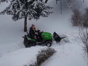 Angela Zinke schiebt Schnee mit kleinem Traktor und lacht in die Kamera.