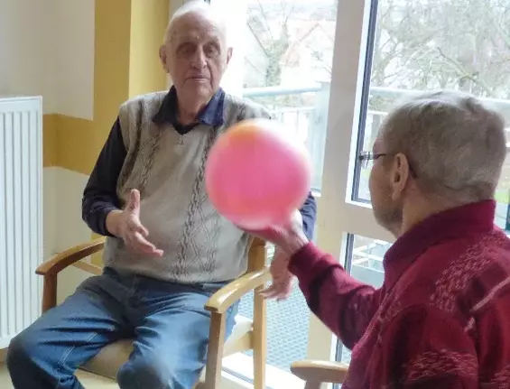 Zwei Senioren werfen sich einen roten Ball zu.