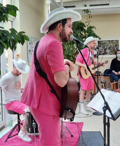 Musiker mit Anzug in Pink, Gitarre und weißem Cowboyhut singt ins Mikro.
