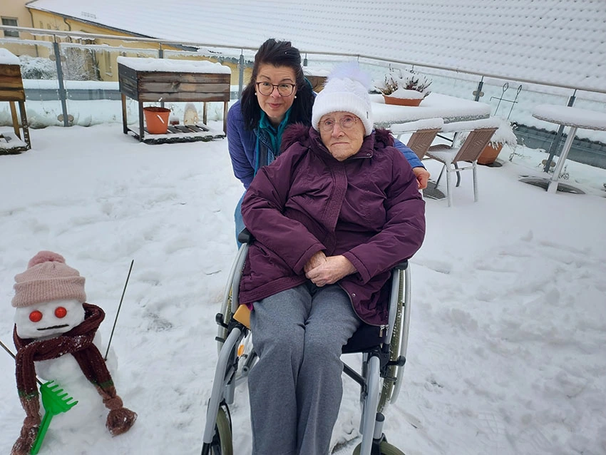 Mitarbeiterin mit Bewohnerin im Rollstuhl auf der verschneiten Terrasse