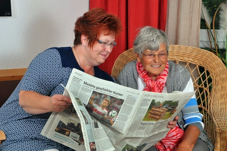 Zwei Frauen sitzen beisammen und lesen dieselbe Zeitung