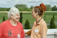 Eine Bewohnerin und eine Pflegerin unterhalten sich im Freien, im Hintergrund sieht man Felder.