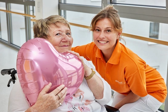 Altenpflegerin und Bewohnerin halten einen Herzluftballon