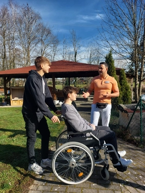 Die Praktikanten Marc und Anthony zusammen mit Fabrice Prieto vom Sozialen Dienst im Garten der Einrichtung. Einer der beiden Schüler lässt sich vom anderen im Rollstuhl schieben, so werden Situationen durchgespielt und Einfühlungsvermögen gefördert.