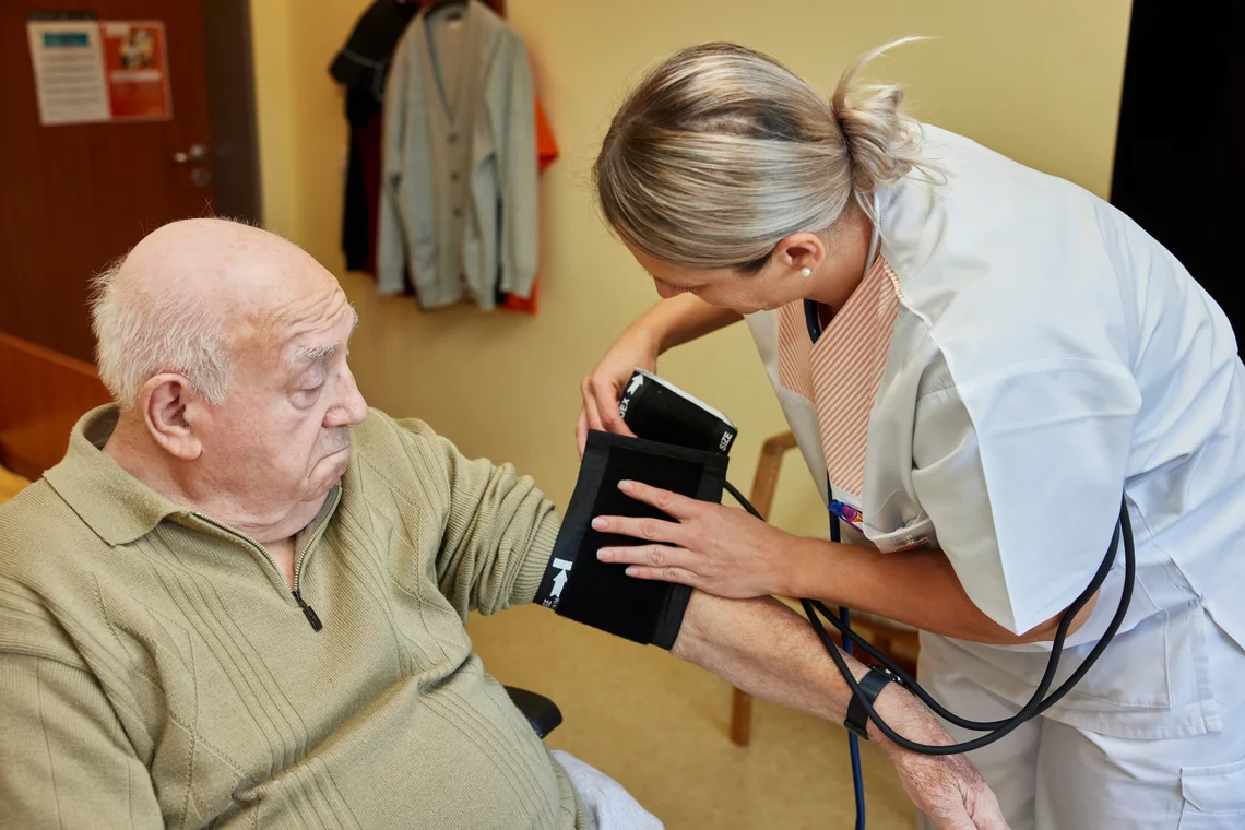 Eine Mitarbeiterin legt einem Bewohner die Manschette zum Blutdruckmessen an.