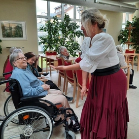 Die Märchenerzählerin zeigt einer Bewohnerin im Rollstuhl einen Gegenstand.