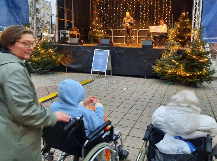 Zwei Bewohner im Rollstuhl mit Begleitung vor der Bühne