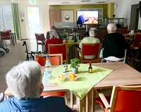 Bewohnerinnen und Bewohner sehen in der Cafeteria einen Film auf einer Leinwand