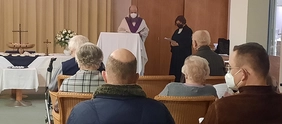 Seniorinnen und Senioren hören beim ökumenischen Gottesdienst die beiden Pfarrer, die neben dem Altar stehen.