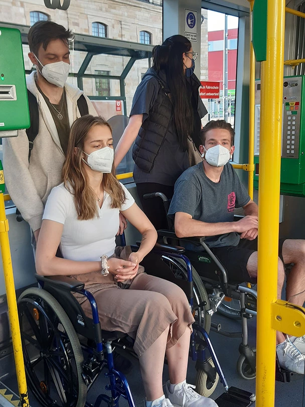 Vier Azubis, zwei davon im Rollstuhl, in der Straßenbahn beim Rollstuhltraining.
