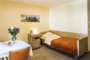 Zimmer mit Bett, Bettschrank, Bild an der Wand, Tisch mit Blumenvase