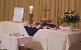 Geschmückter Altar mit Kerze, Kreuz, einem Boot, Blumen und Steinen.