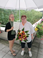 Rita Balan mit Verwaltungskraft Hanna Ewert, die Blumen und Urkunde übergibt