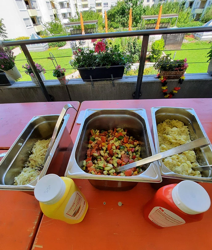 Salat und Bratwurst stehen auf einem Tisch auf der Terrasse des Wohnbereichs bereit.