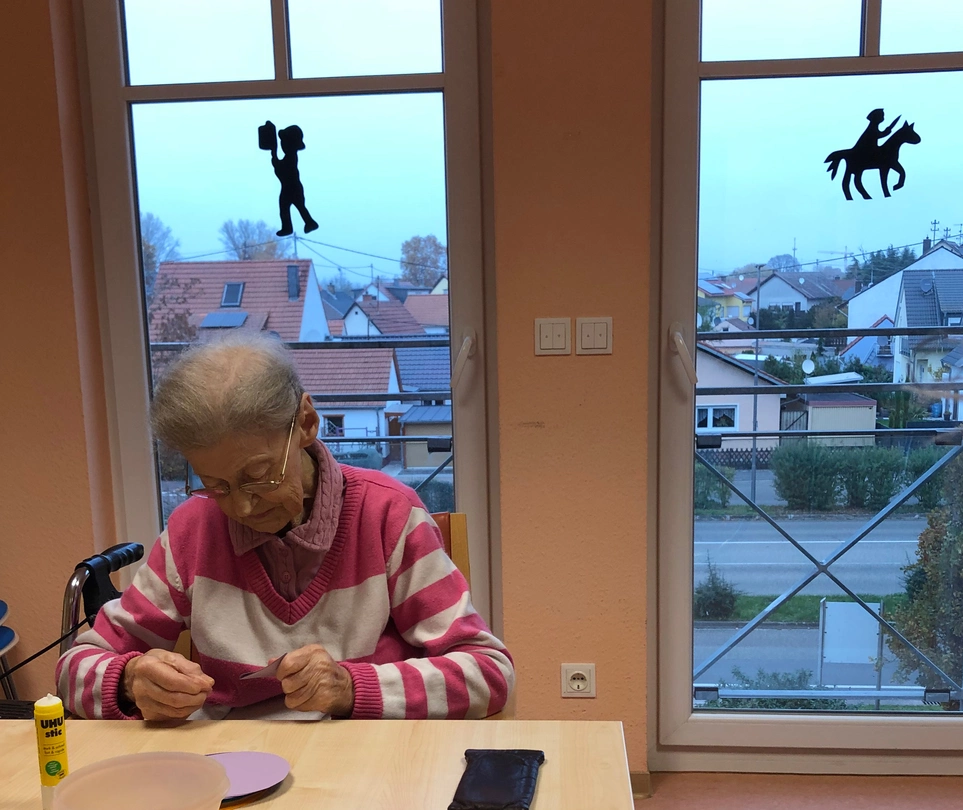 Eine Bewohnerin schneidet eine Vorlage aus, im Hintergrund hängen schon Fensterbilder.