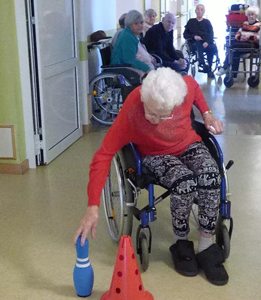 Eine Frau im Rollstuhl bückt sich nach einem Kegel.