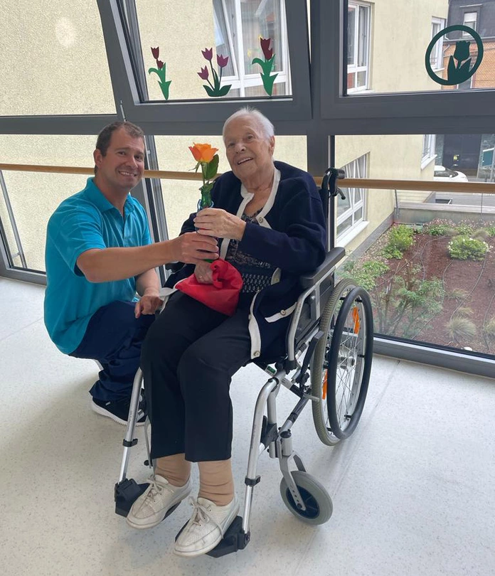 Mitarbeiter Antonio überreicht eine Rose an eine Bewohnerin im Rollstuhl