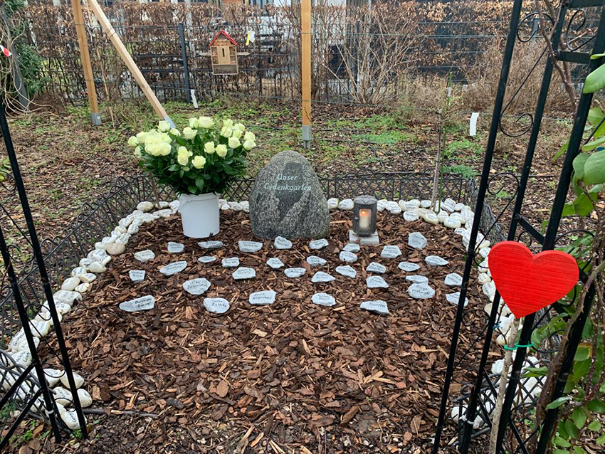 Blick in den Gedenkgarten, eine Stelle im Garten, an der an einem Rosenbogen Steine mit den Namen der Verstorbenen niedergelegt wurden. 